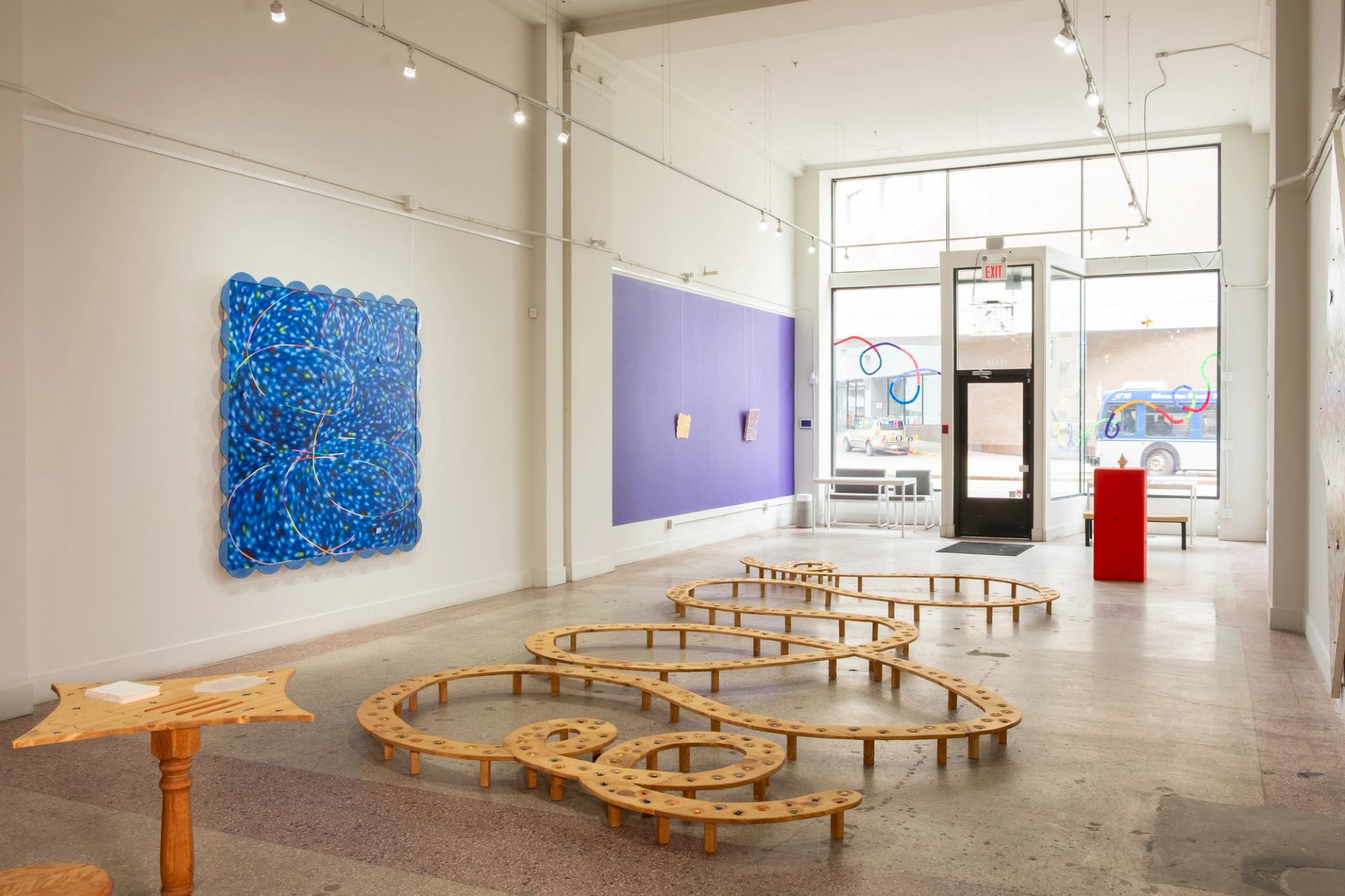 White walled gallery is brightly lit, with large colourful paintings on the wall.