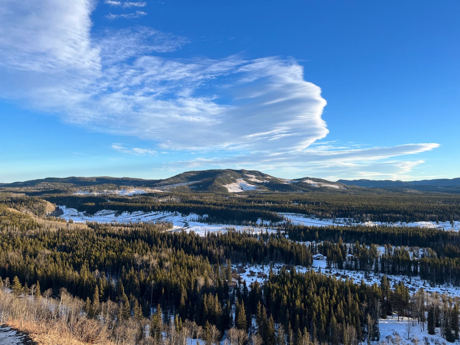 Sweeping foothills landscape with forests, snow patches, and dramatic cloud formations.