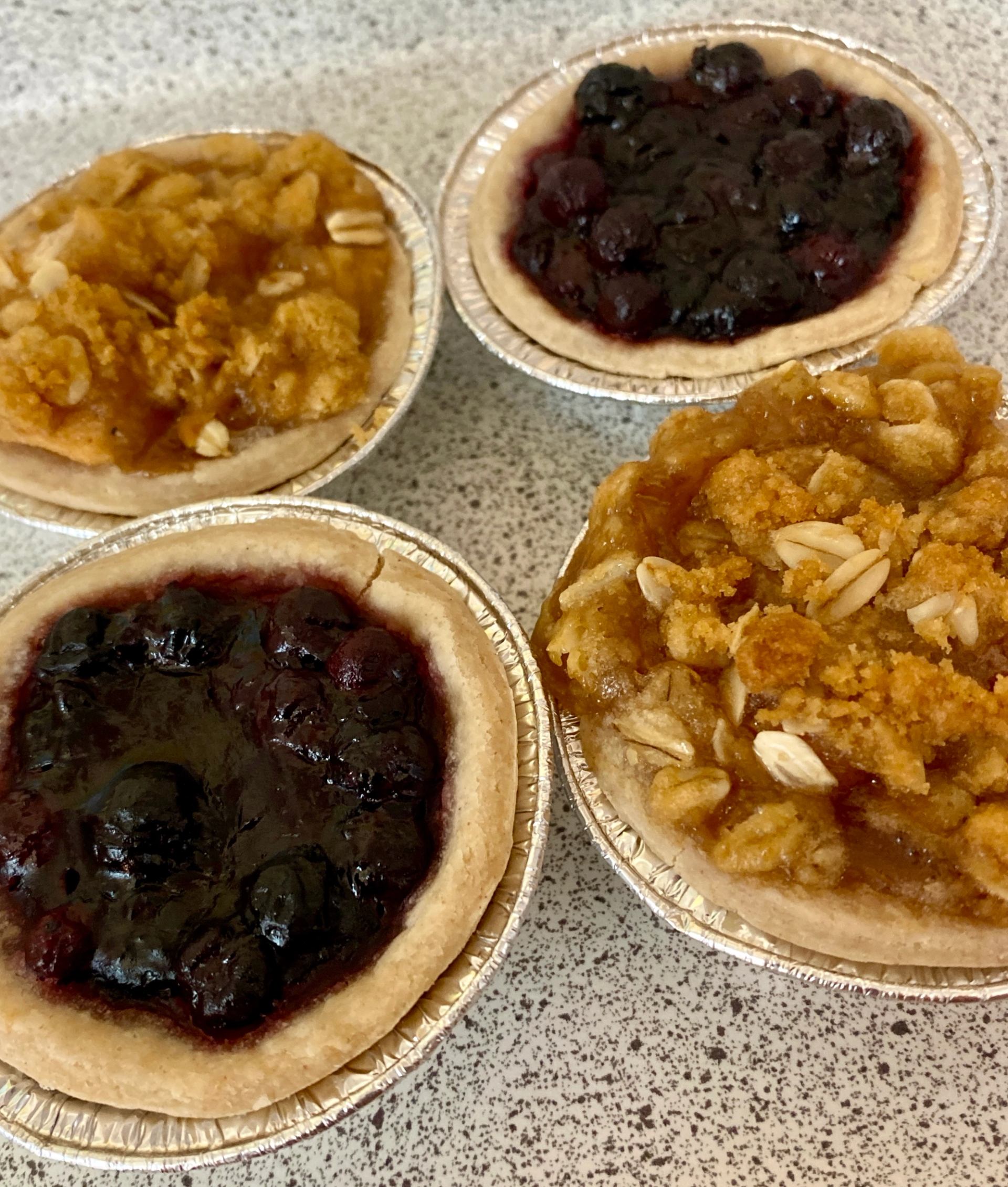 Four mini pies with fruit fillings on a countertop.
