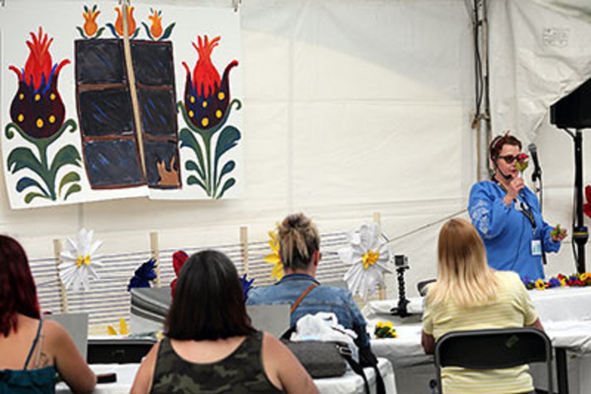 Instructor leading a craft workshop with attendees seated inside a festival tent.