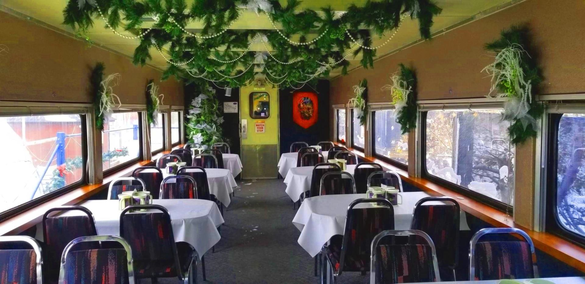 Dining car with white-clothed tables, dark chairs and evergreen garlands.