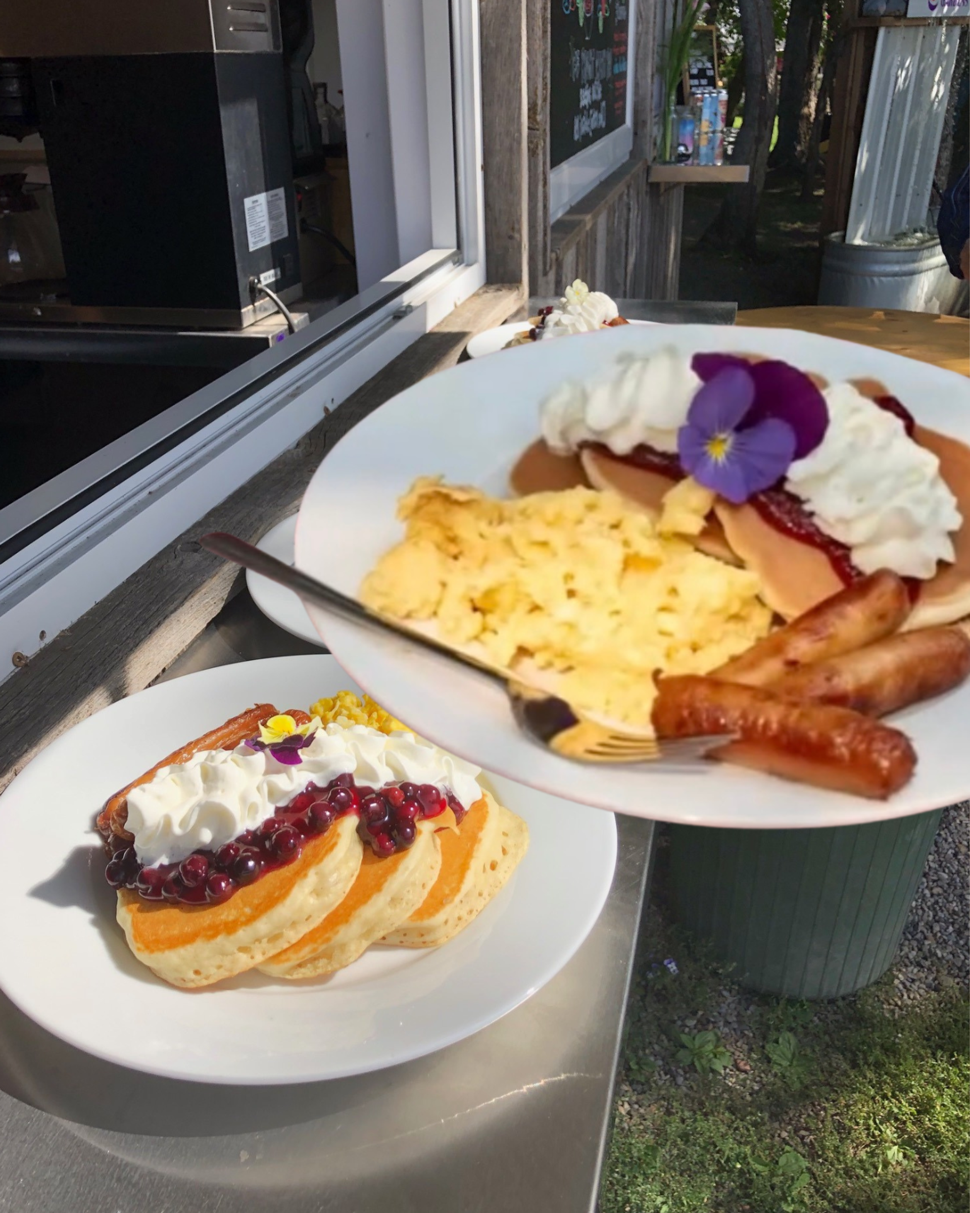 Plates of pancakes with whipped cream, berries, scrambled eggs and sausages at outdoor counter