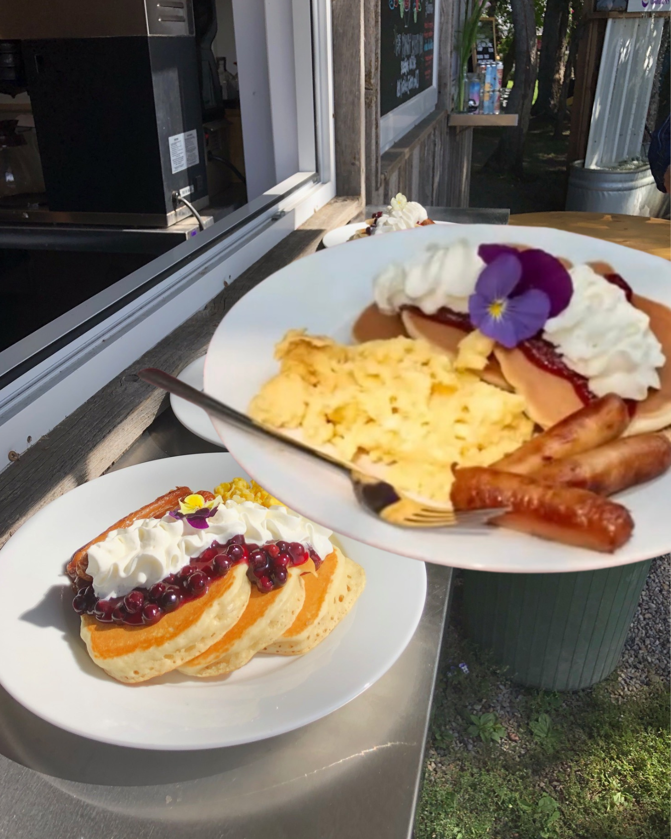 Plates of pancakes with whipped cream, berries, scrambled eggs and sausages at outdoor counter