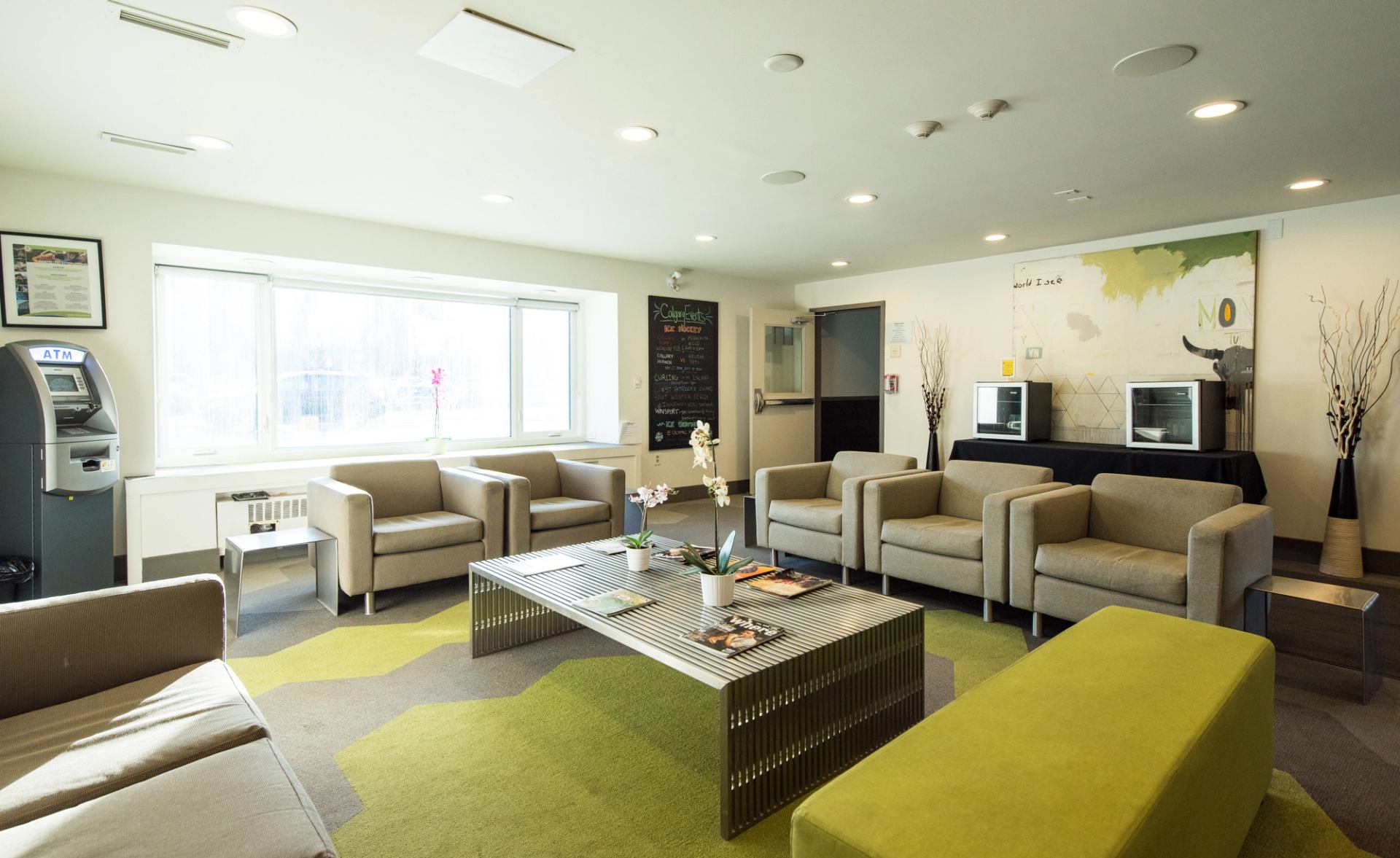 Modern hostel lounge with beige seating, glass table, and colorful wall decor.