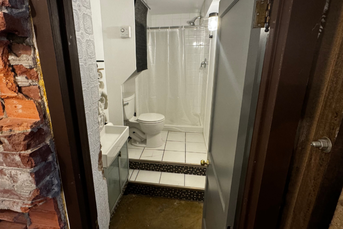 Small bathroom with raised tiled floor, toilet, shower, and exposed brick wall at entrance.