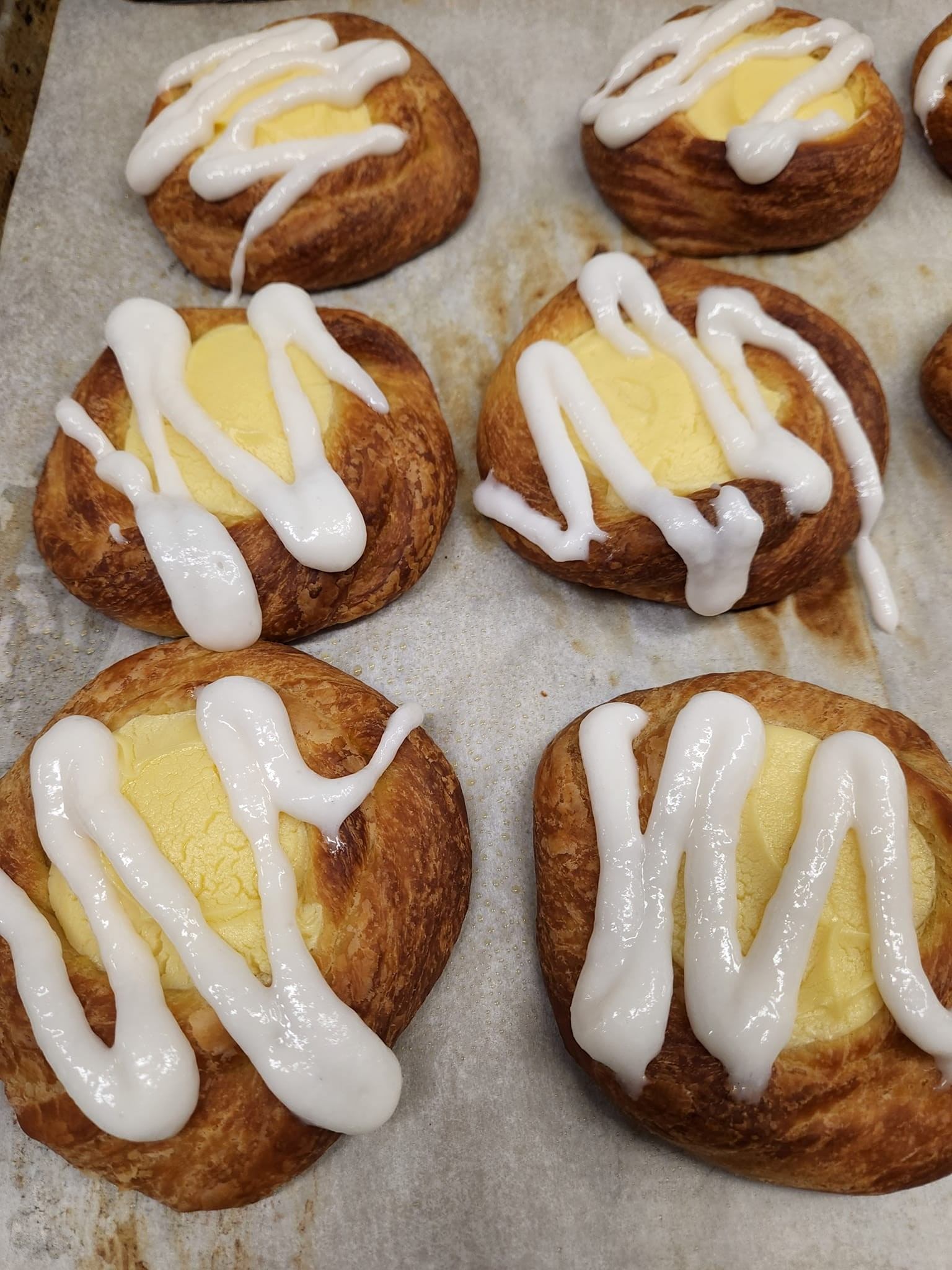 Butter tarts with white icing drizzle on parchment paper, close-up view of four pastries.