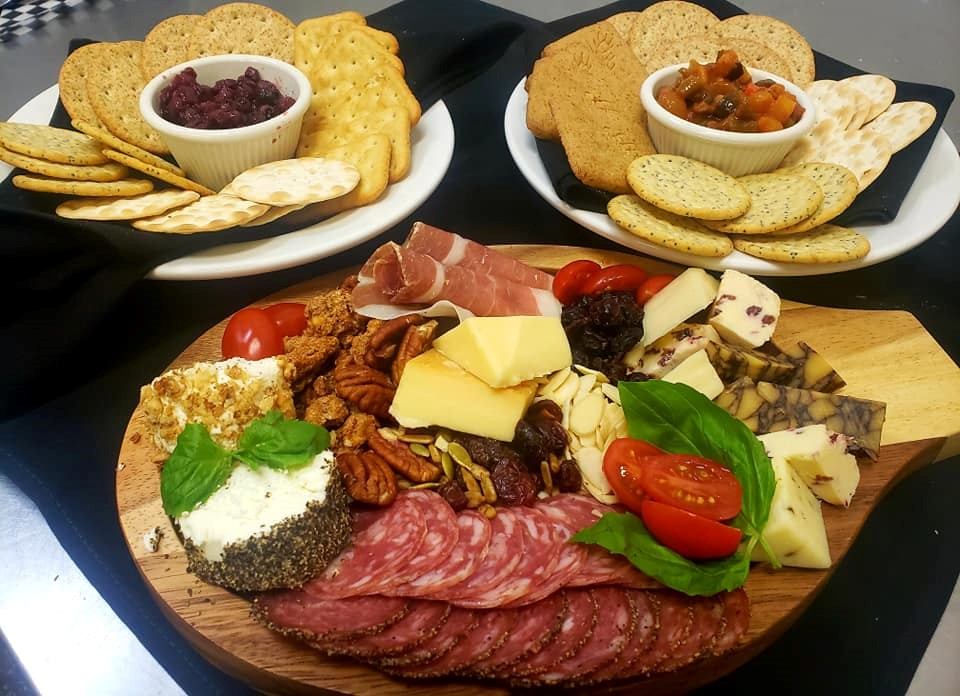 Charcuterie platter with sliced salami, cheese, olives, crackers, and two bowls of dips.
