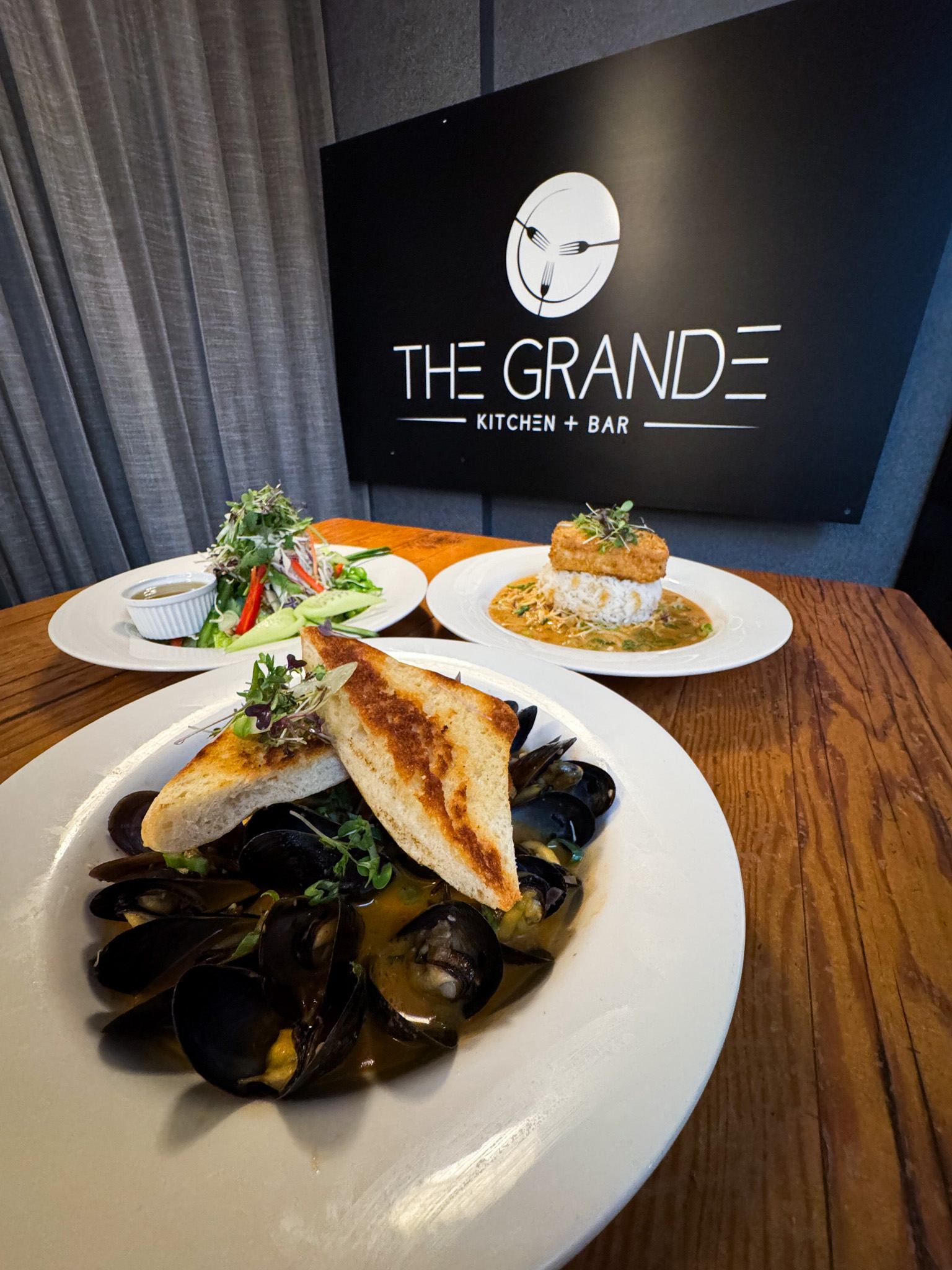 Gourmet dishes with The Grande Kitchen + Bar sign in the background.