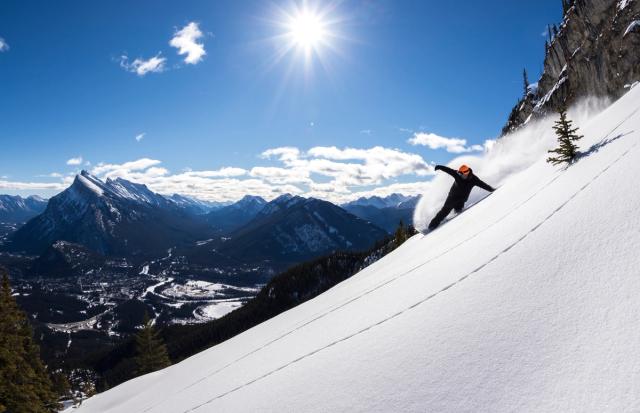 A snowboarder carves and creates a snow spray while snowboarding at Mt. Norquay Ski Resort in Banff National Park