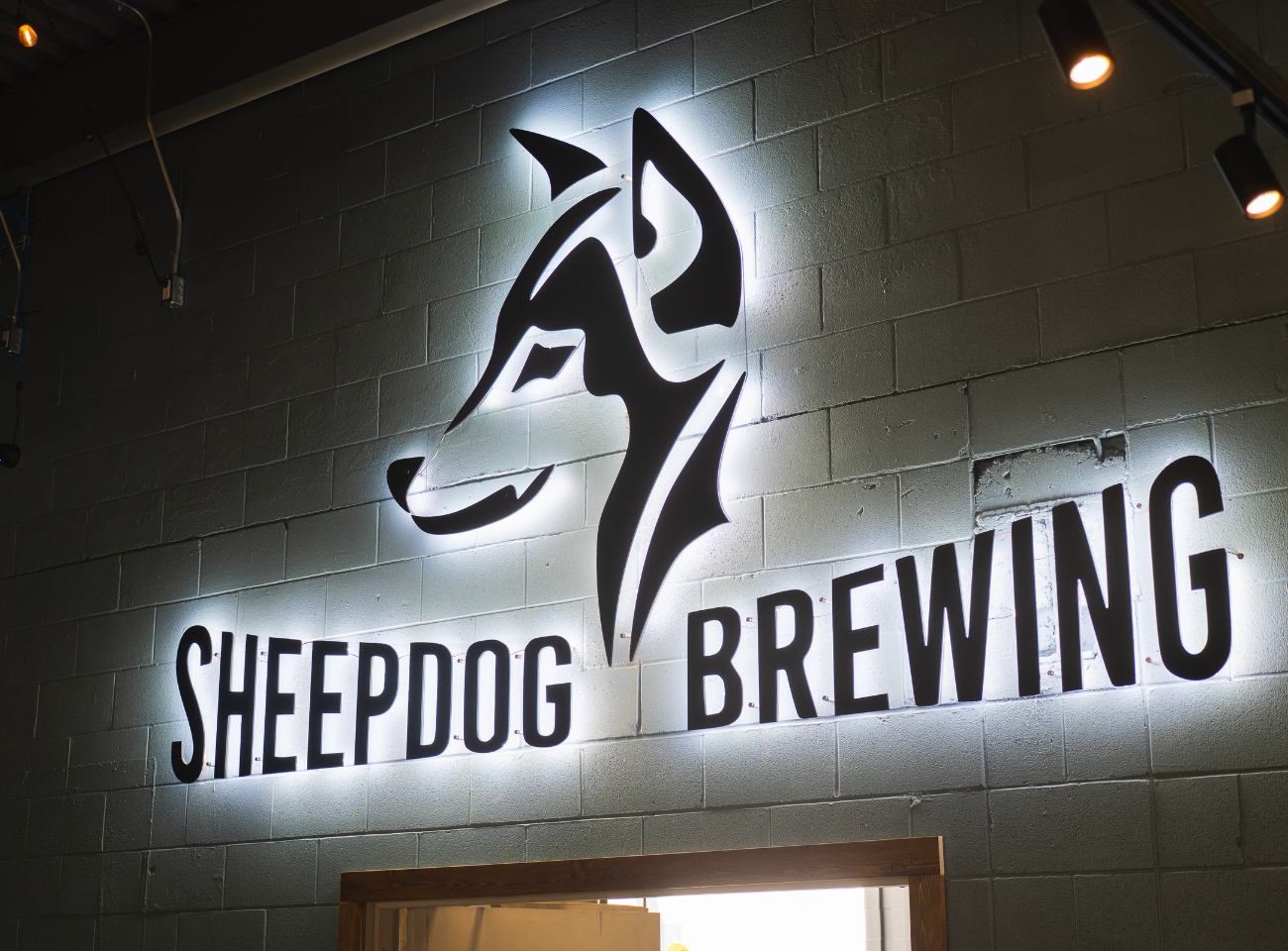 Illuminated Sheepdog Brewing logo and dog graphic on a grey brick wall.