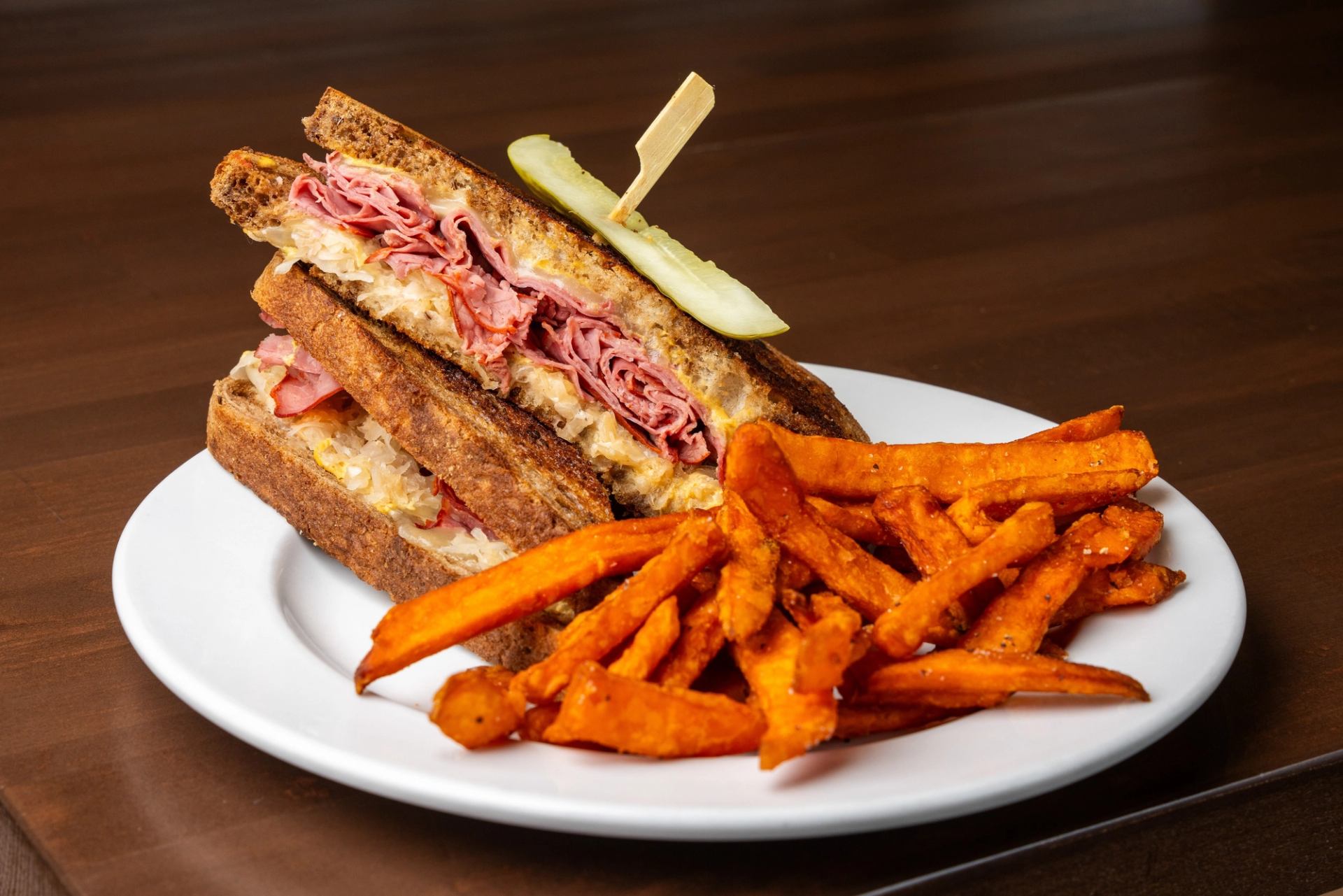 A loaded deli sandwich served with sweet potato fries and a pickle.