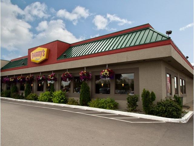 Exterior of Denny’s restaurant with green roof and hanging flower baskets.