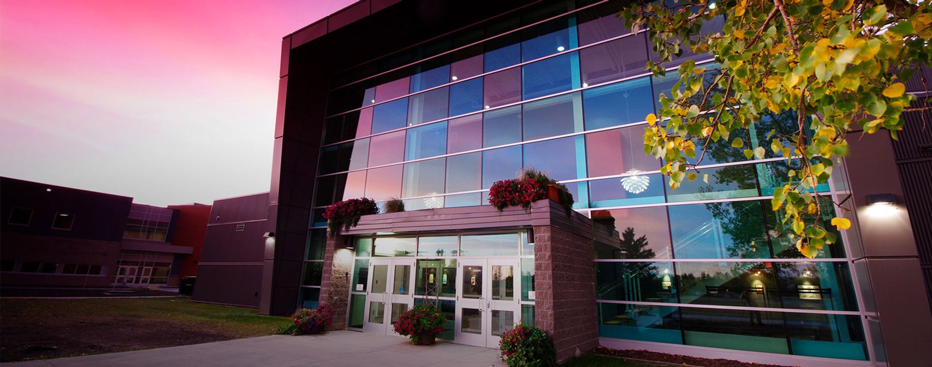 Modern glass-front theatre building at sunset with flowers and trees