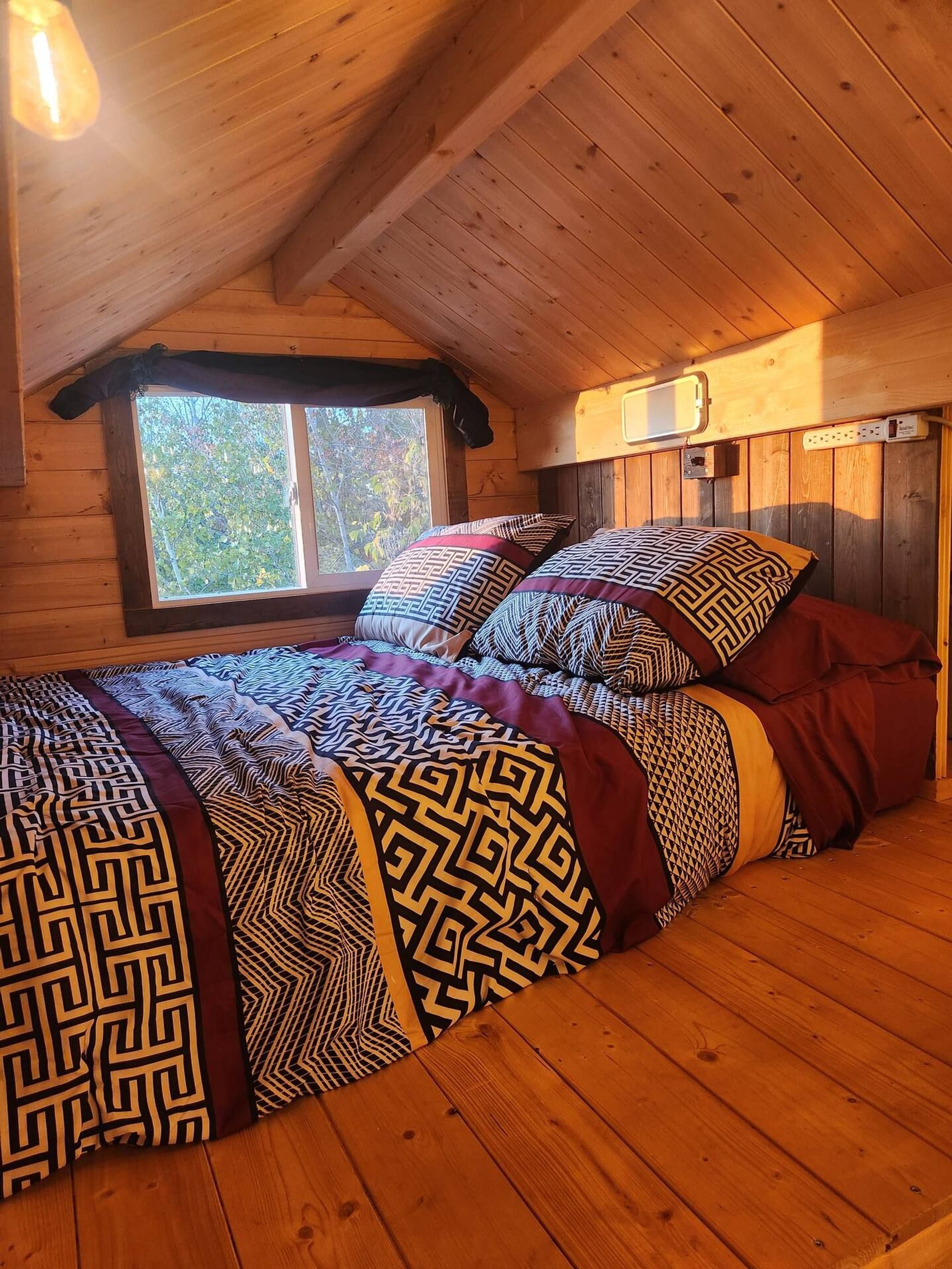 Loft bedroom with patterned bedding and a window overlooking trees.