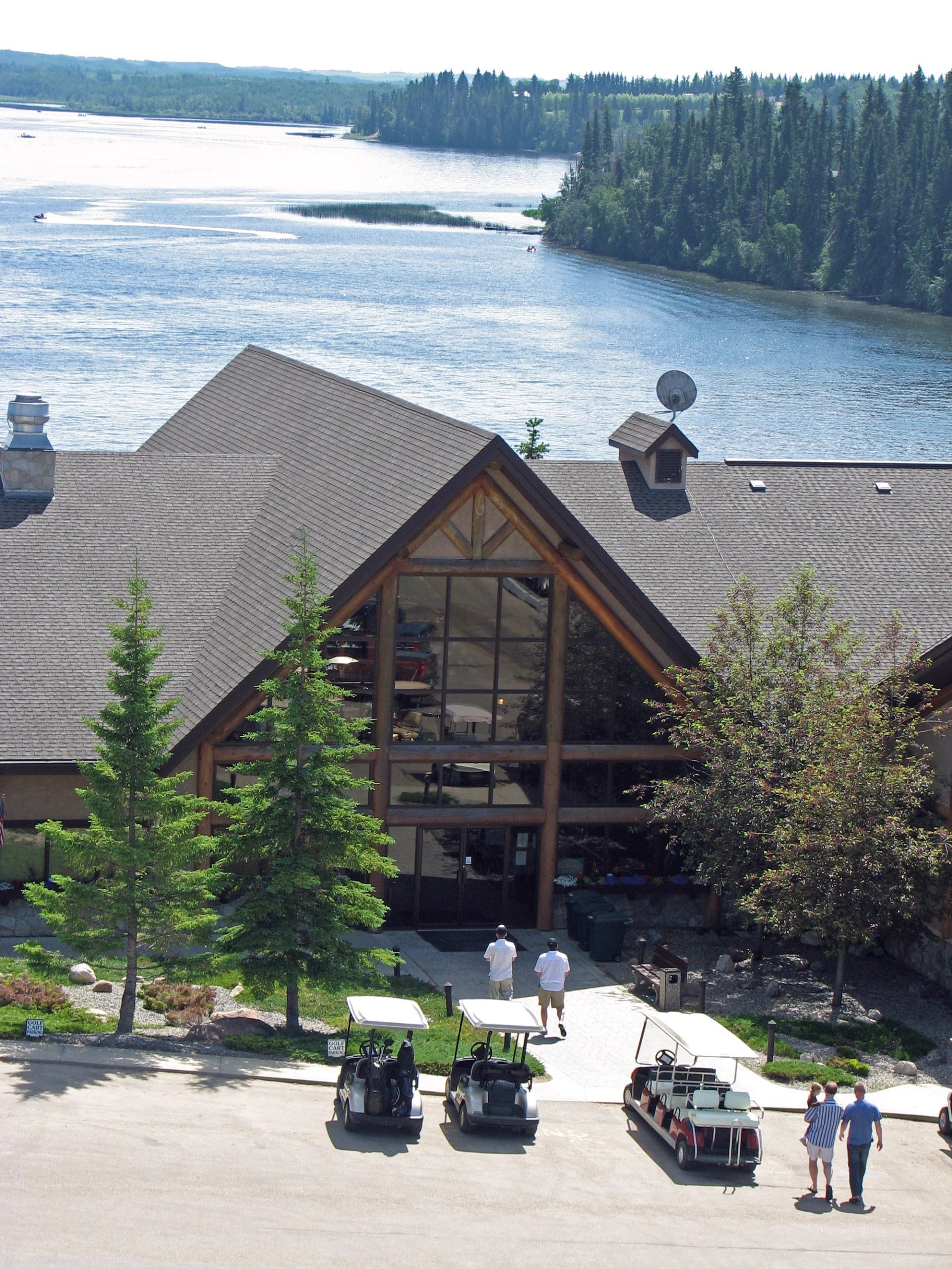 Lakeside lodge with large windows, parked golf carts, and people walking on path.