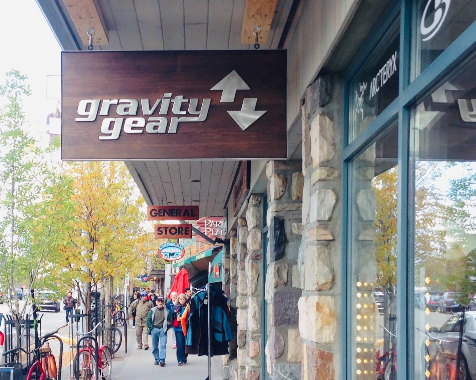 Gravity Gear store sign on a busy street with shoppers, bikes, and autumn trees.