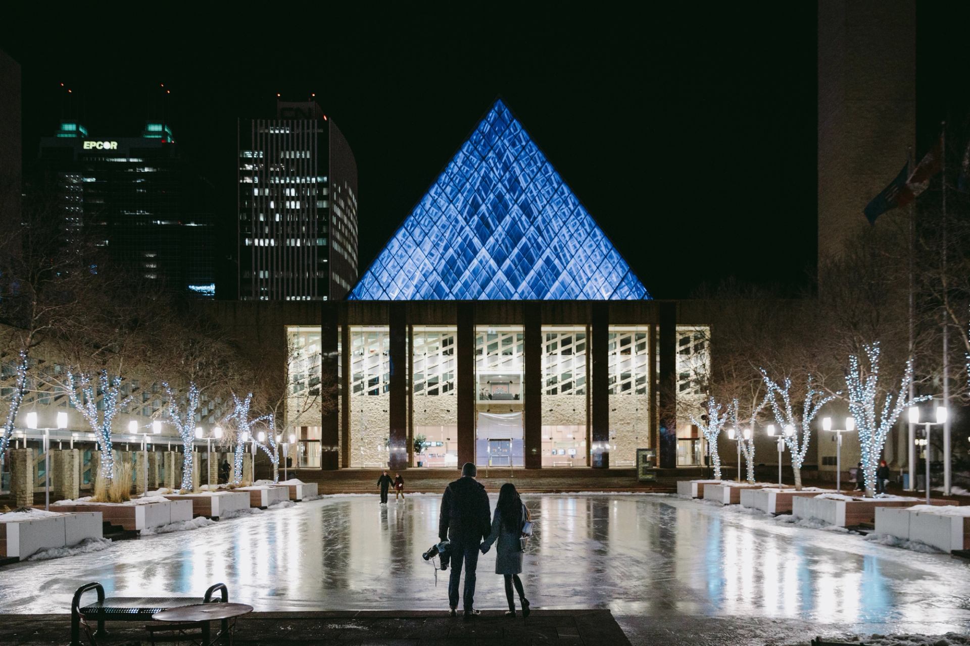 Edmonton City Hall at night with illuminated blue pyramid and office towers in background.