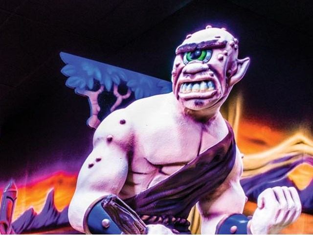 Cyclops creature figure with blue wings, clenched fist, glowing mural background.