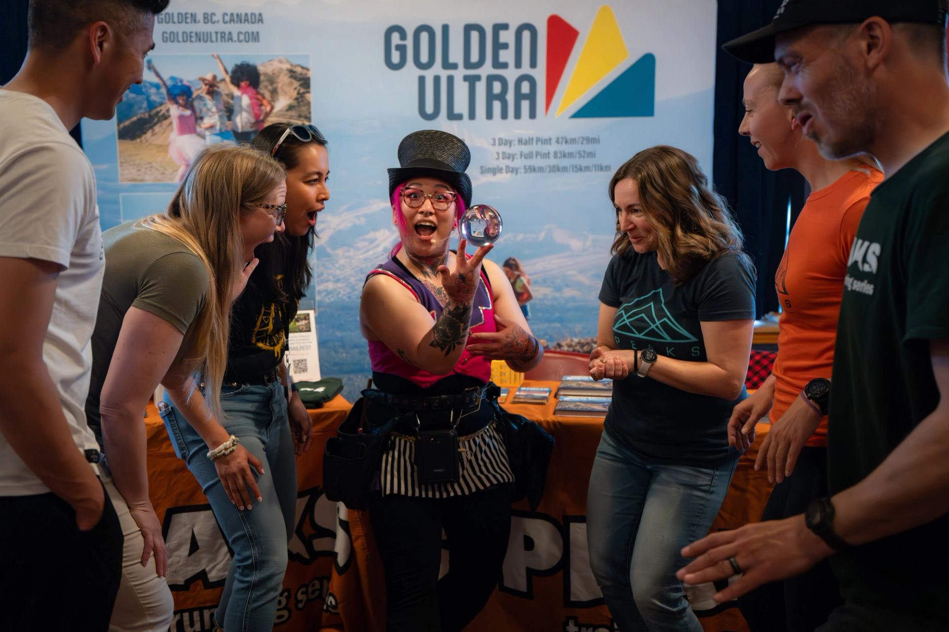 Performer with top hat shows crystal ball trick to group at Golden Ultra booth.
