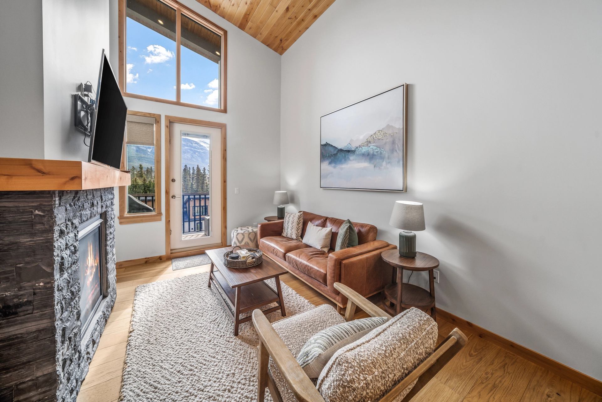 Living room with leather sofa, fireplace, large windows and mountain view outside.