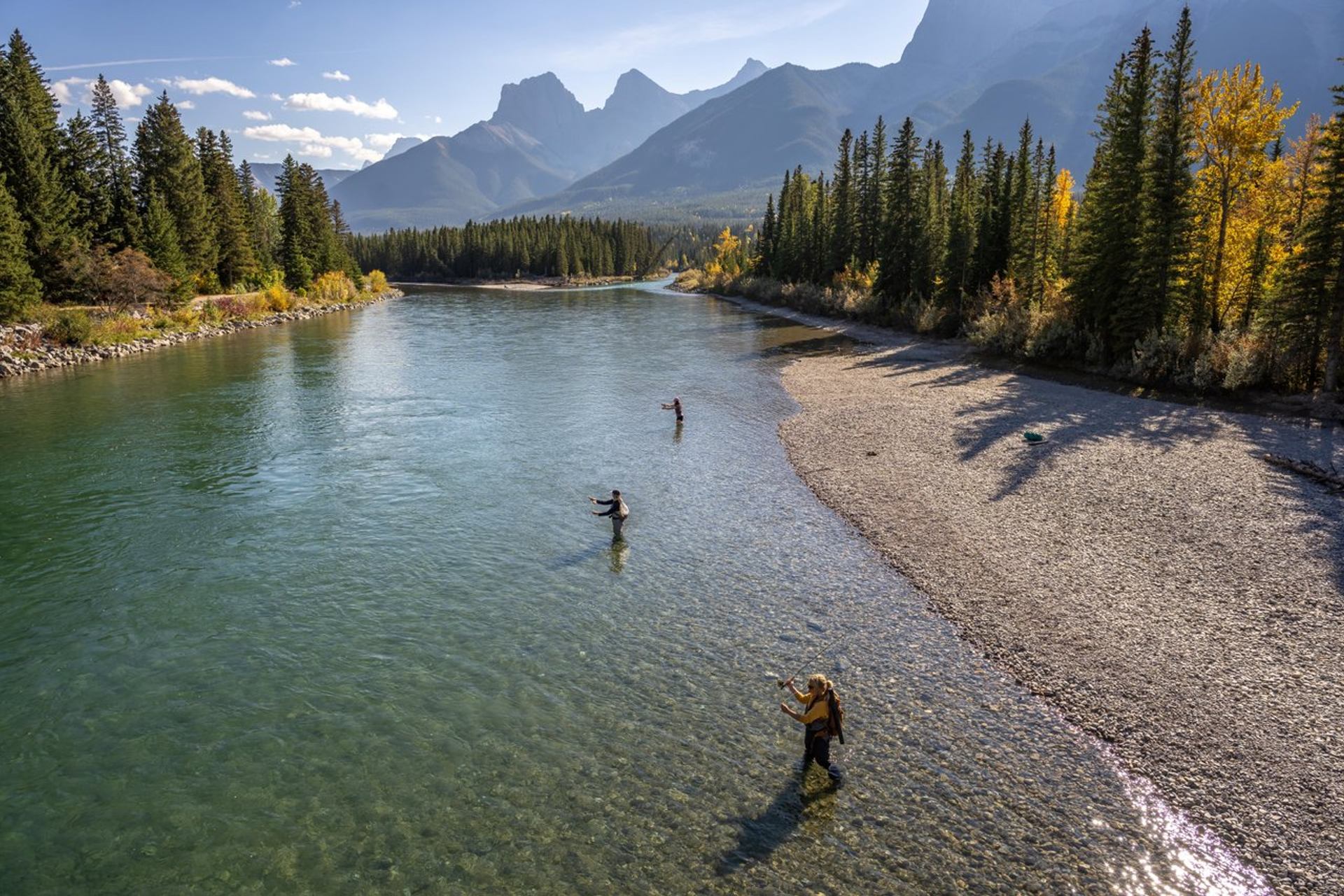 People fishing in the Bow River with the Three Sisters Mountains in the background