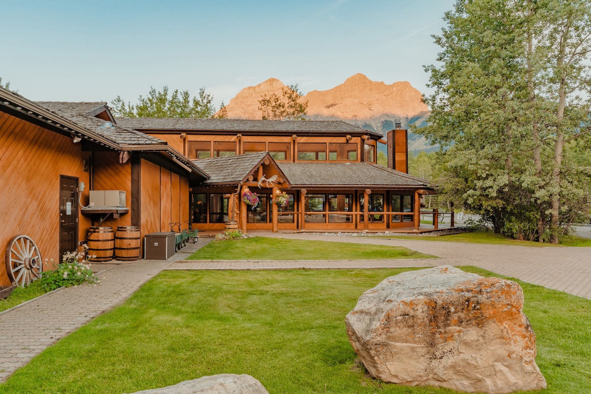 Wooden ranch buildings with a manicured lawn and tall mountain peaks in the background.