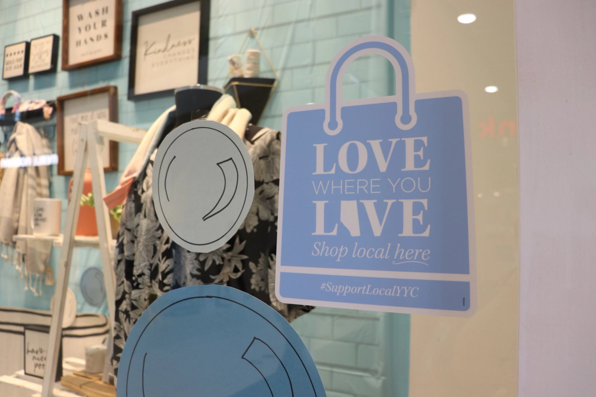 Storefront with “Shop Local” sign and display of clothing and framed art.