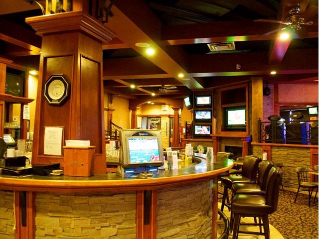 Curved bar counter with stools, wood columns, and TV screens in lounge.