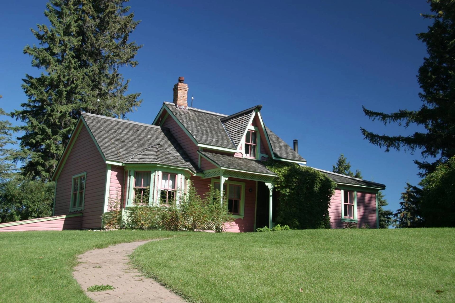 Pink historic house with green trim, set in greenery and tall trees.