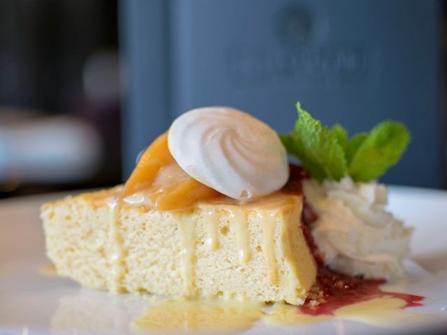 Cheesecake topped with fruit, whipped cream, and mint on a white plate.
