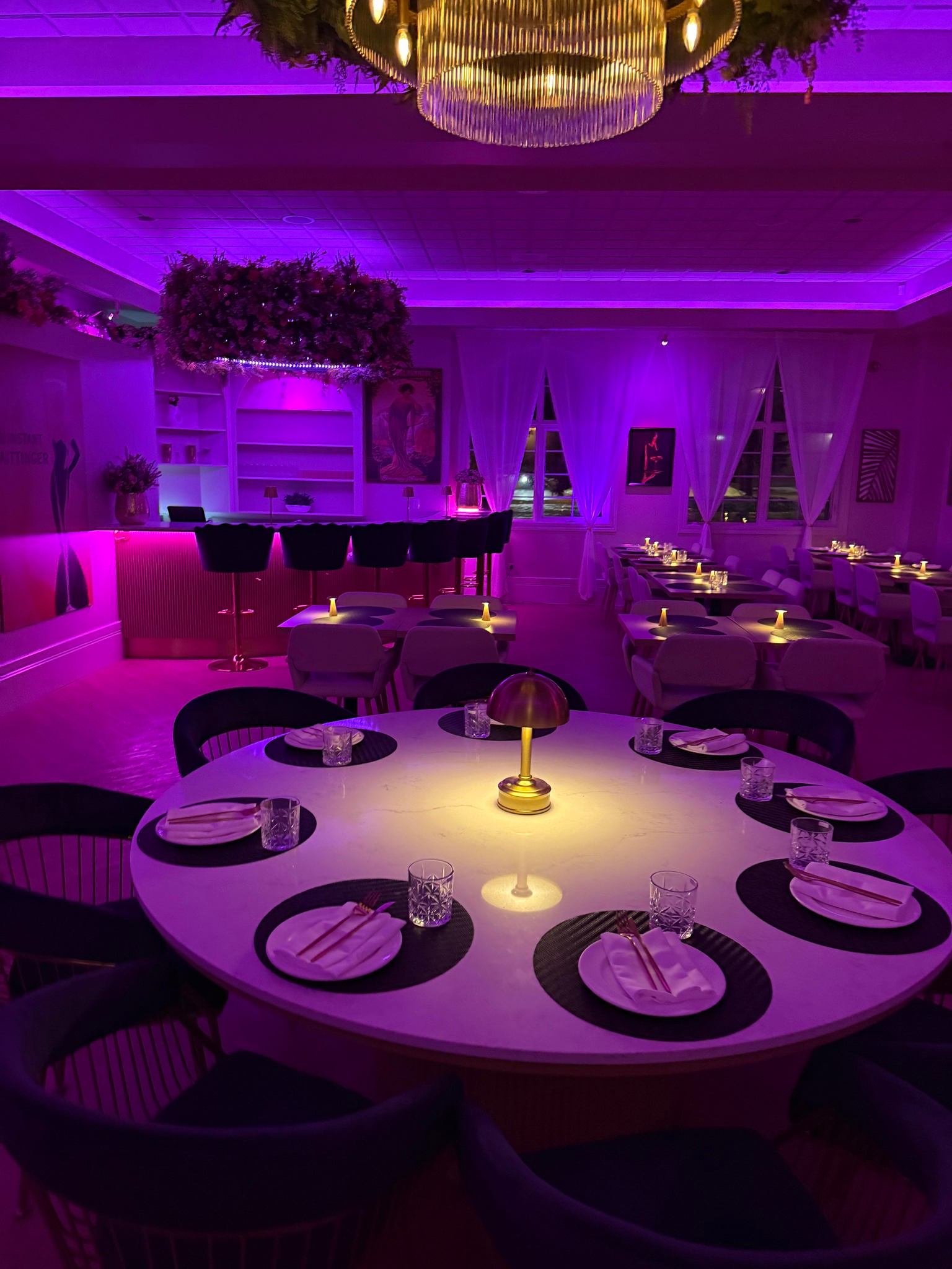 Round dining table with candles and plush chairs under purple lighting at Bungalow Club.