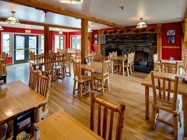 Rustic dining room with wooden tables, red walls, and a stone fireplace.