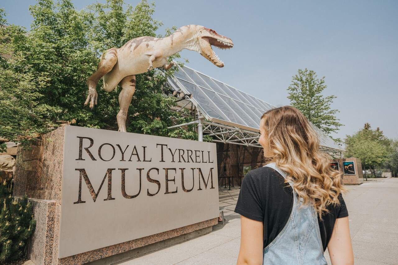 Visitor looks at dinosaur sculpture above Royal Tyrrell Museum sign and entrance.