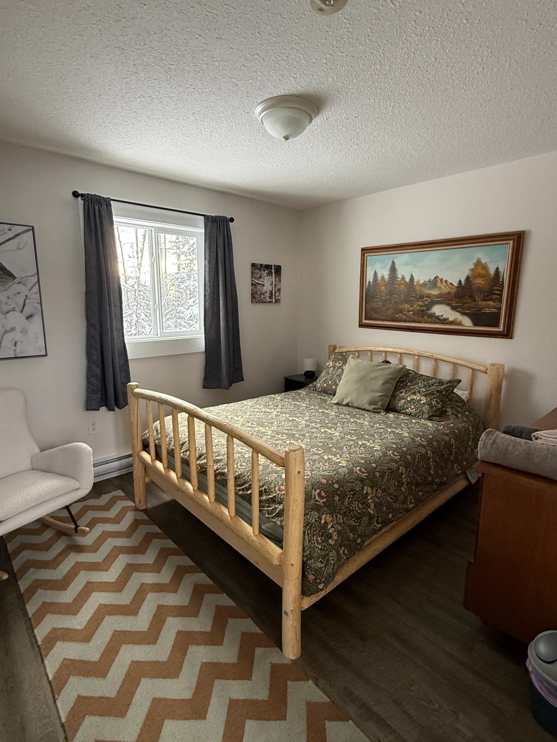 A bedroom with a wooden bed frame, nature‑themed decor, and a window with curtains.