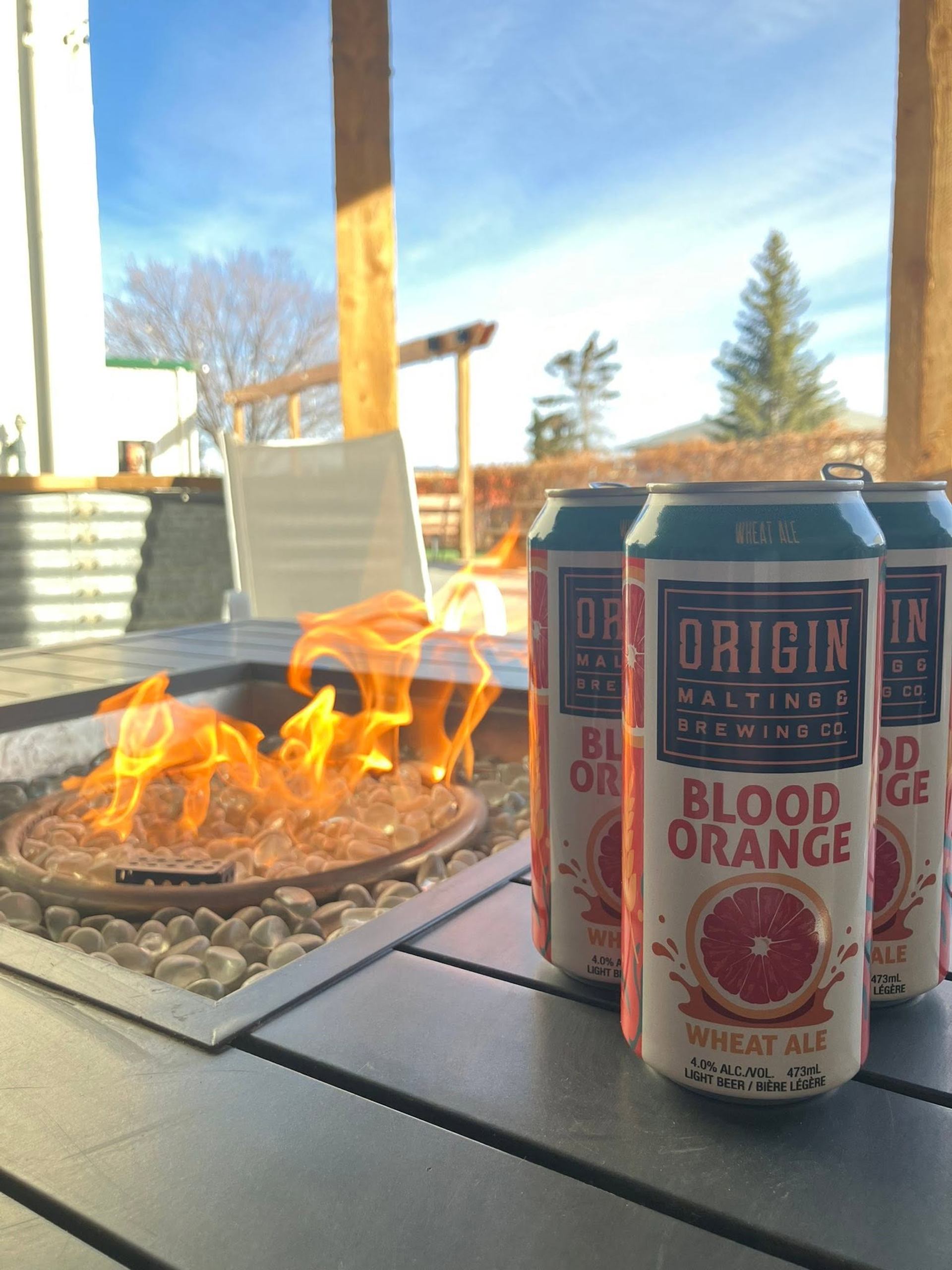 Several beverage cans sit beside a glowing fire table on an outdoor patio with seating nearby.
