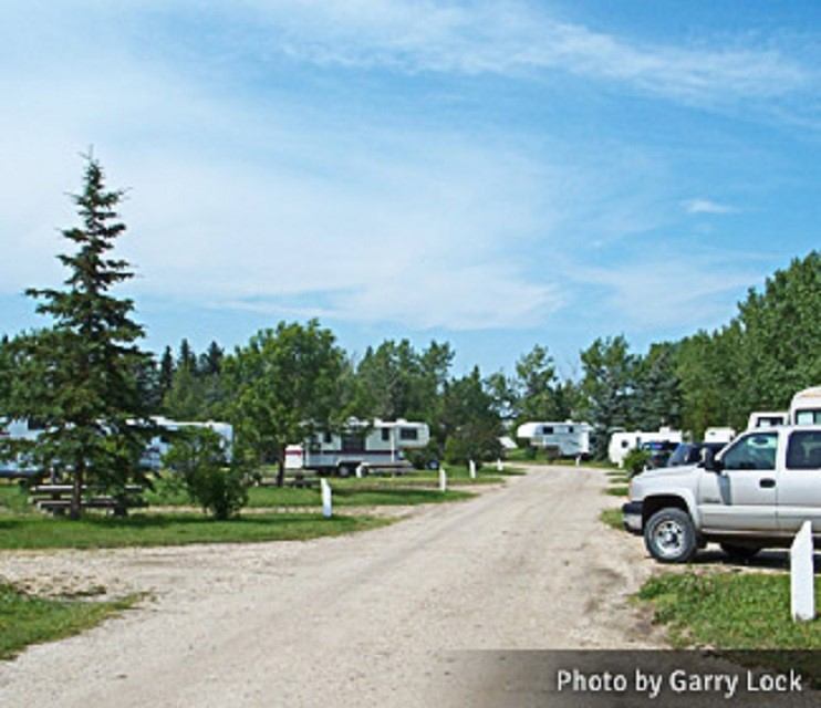 Campground with RVs, trees, and grass under a partly cloudy sky at Beaverlodge Pioneer Campground.