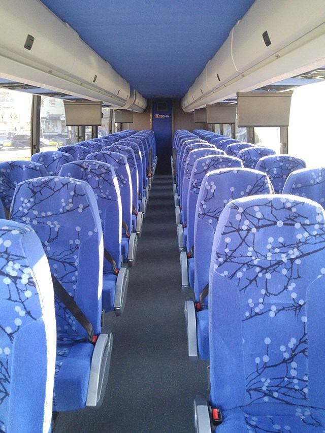 Interior of Ebus with patterned blue seats and overhead compartments.