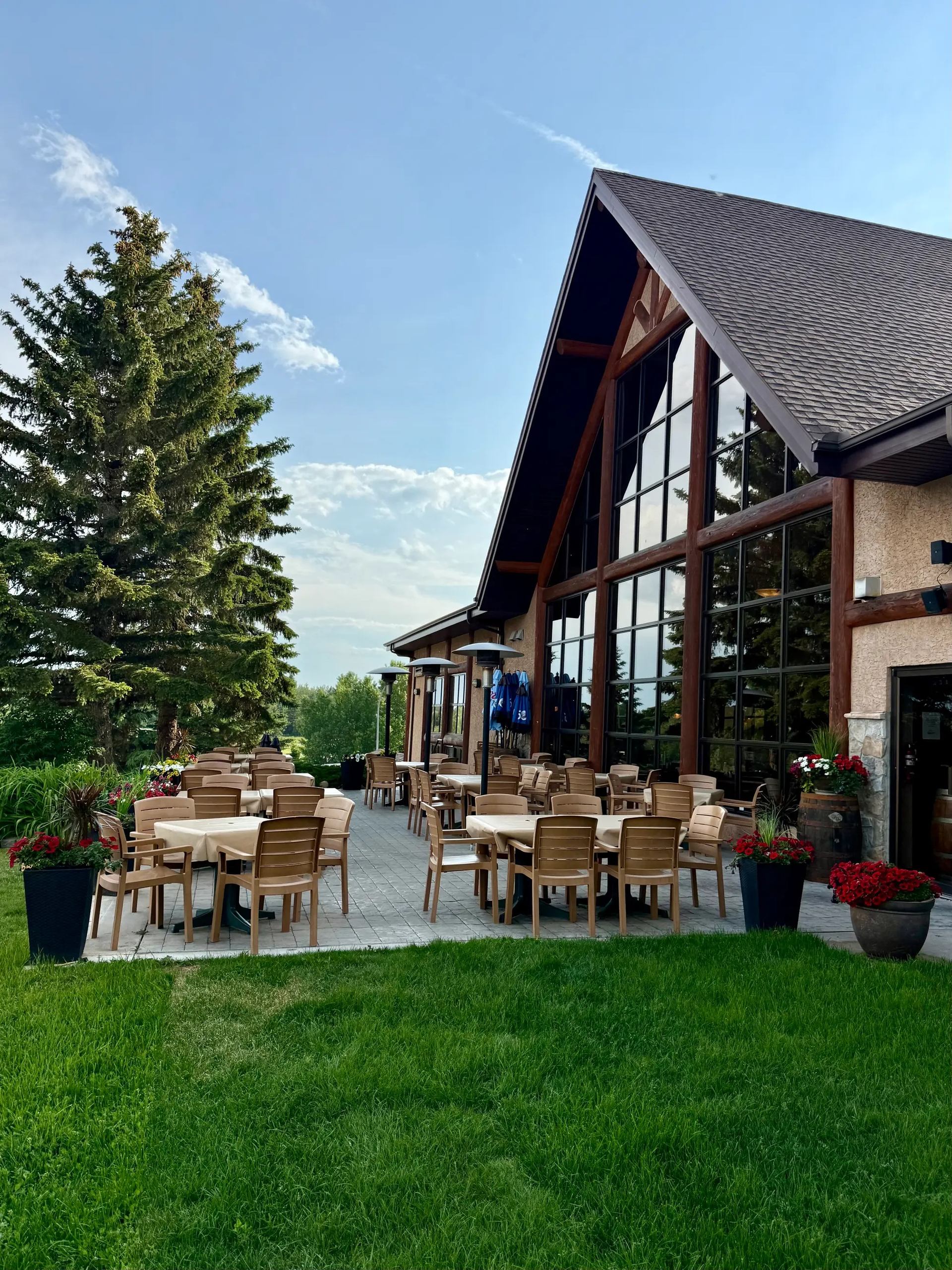 Outdoor restaurant patio with wooden tables beside large glass windows and green lawn.