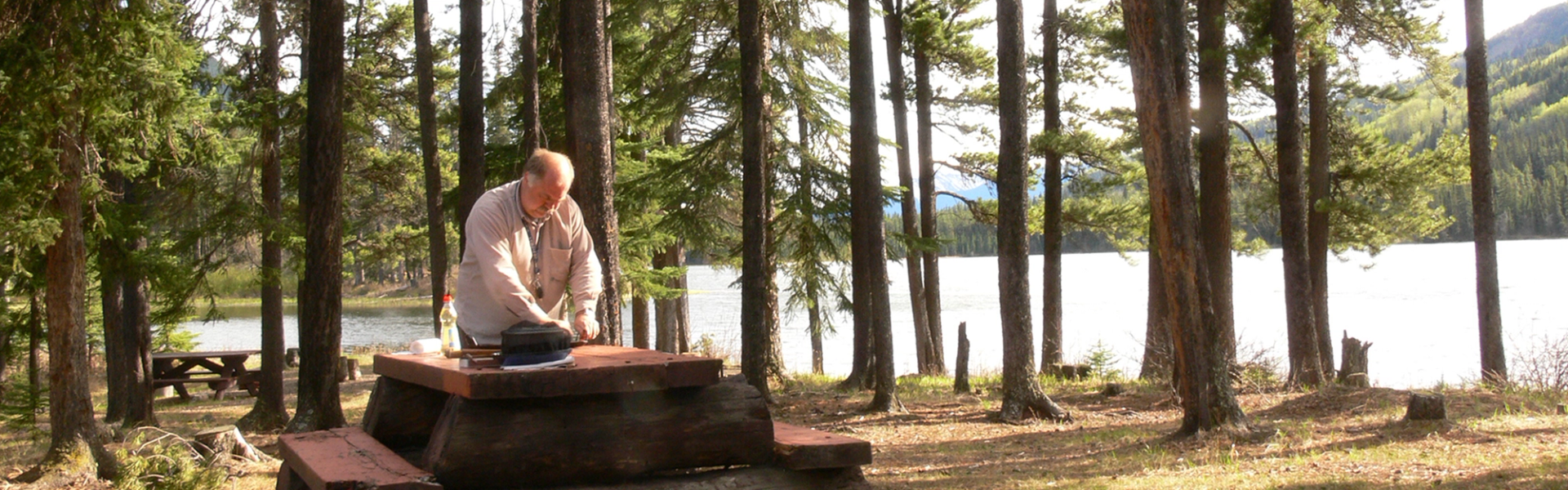 Man cooking on a picnic table at a wooded lakeside campsite in Moberly Flats Campground.