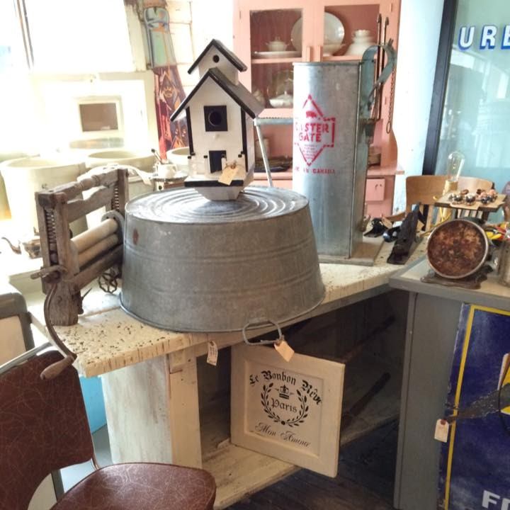 Antique mall display with decorative birdhouse, metal bucket, and sign on shelves.