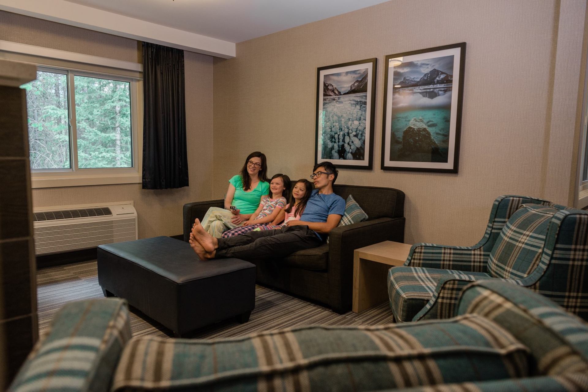 A family of four relaxing on a sofa in a spacious hotel suite watching TV.
