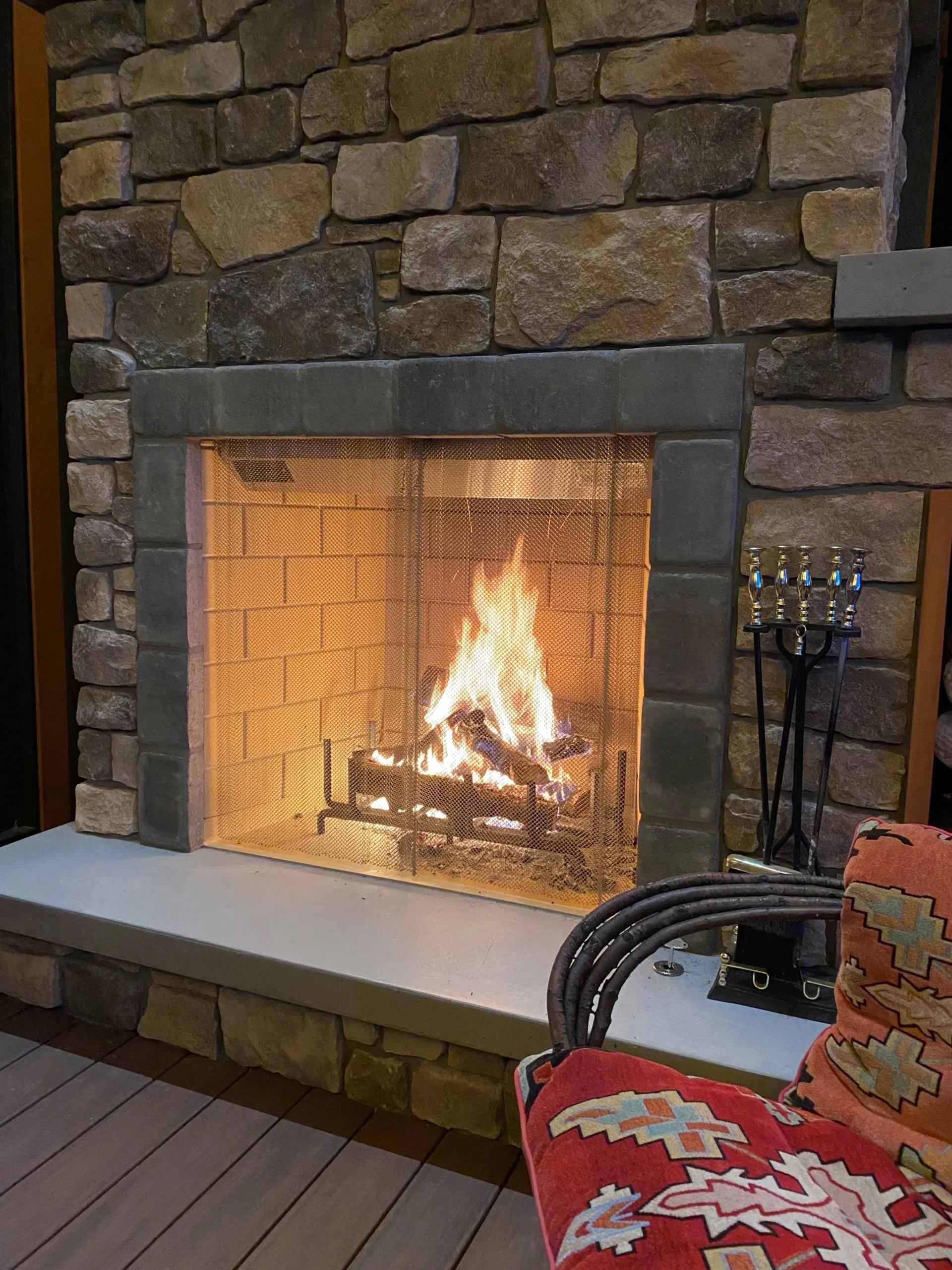 Stone fireplace with glowing fire and cozy red floral armchair.