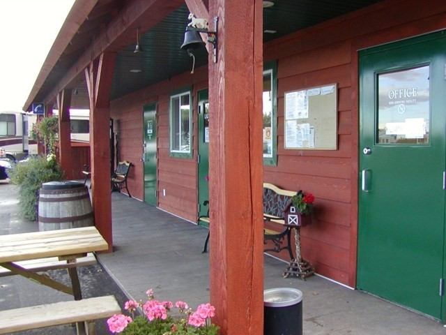 Rustic building with green doors, flowers, bench, and outdoor seating.