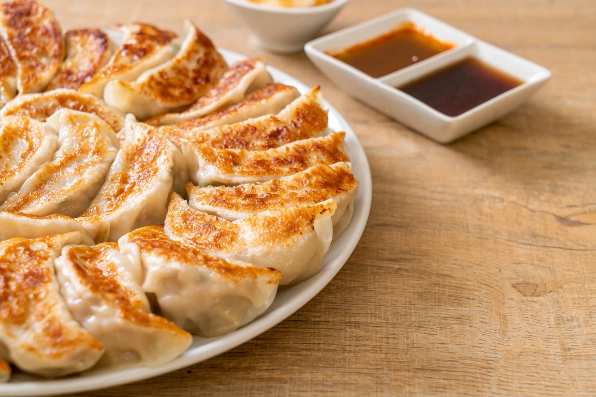 Plate of pan-fried dumplings with dipping sauces on wooden table.