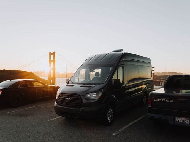 Black campervan parked near bridge at sunset.