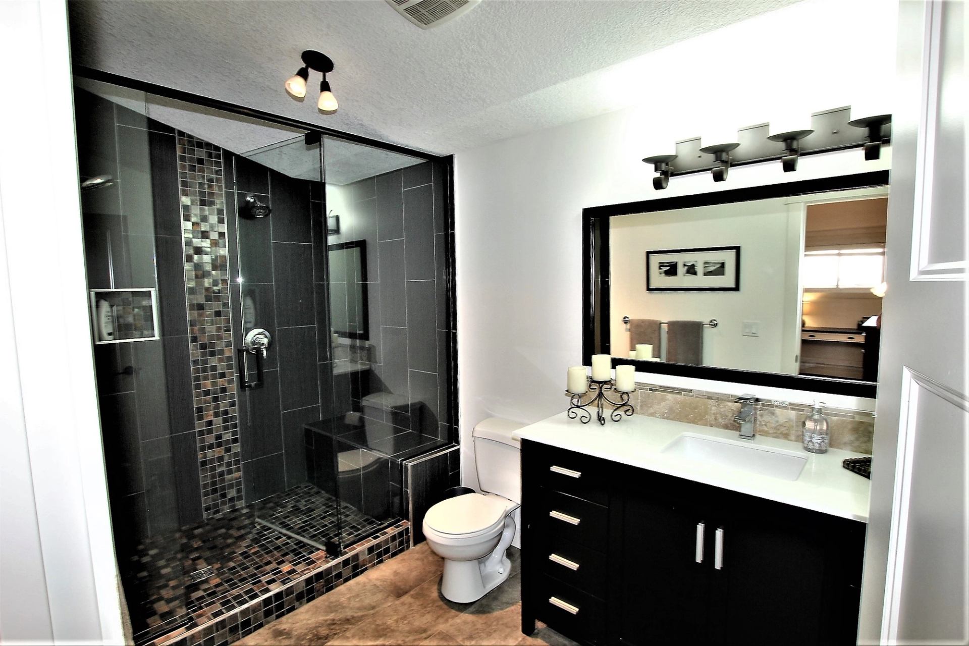 Modern bathroom with glass shower, dark tile, and sleek vanity.