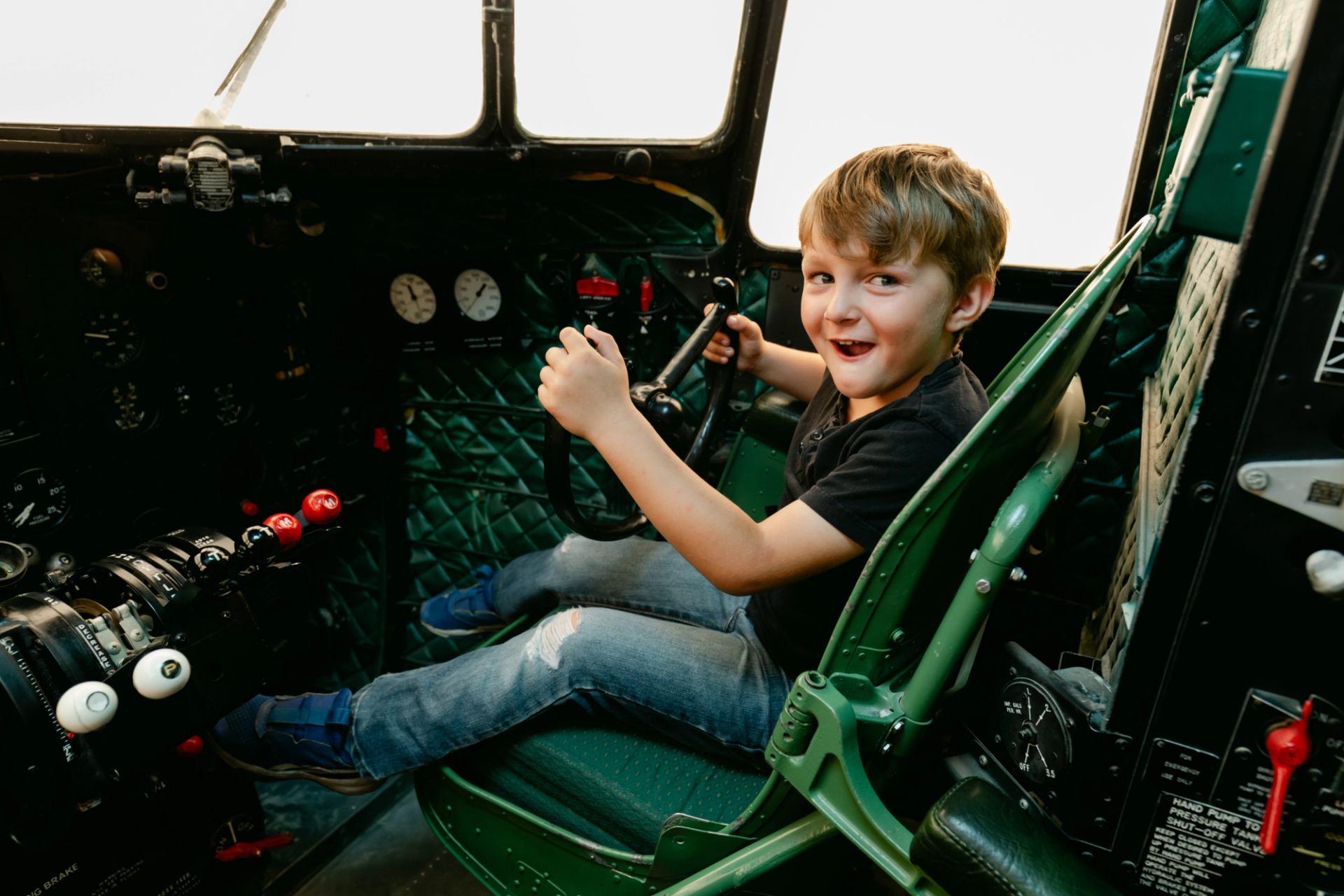 Child sitting in airplane cockpit, holding control yoke among gauges and switches.