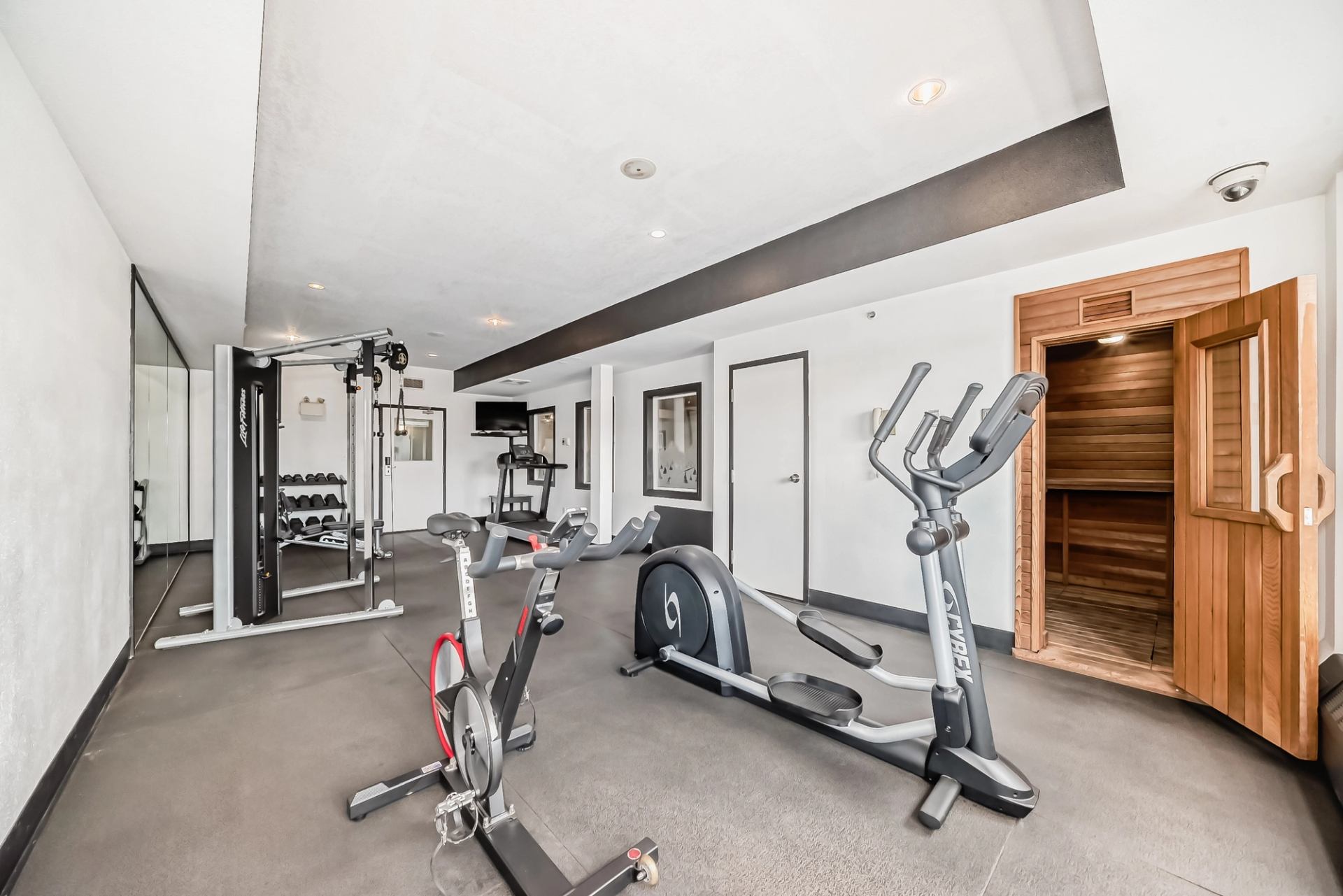Fitness room with cardio machines, weight equipment, and sauna door at Grande Cache Inn.