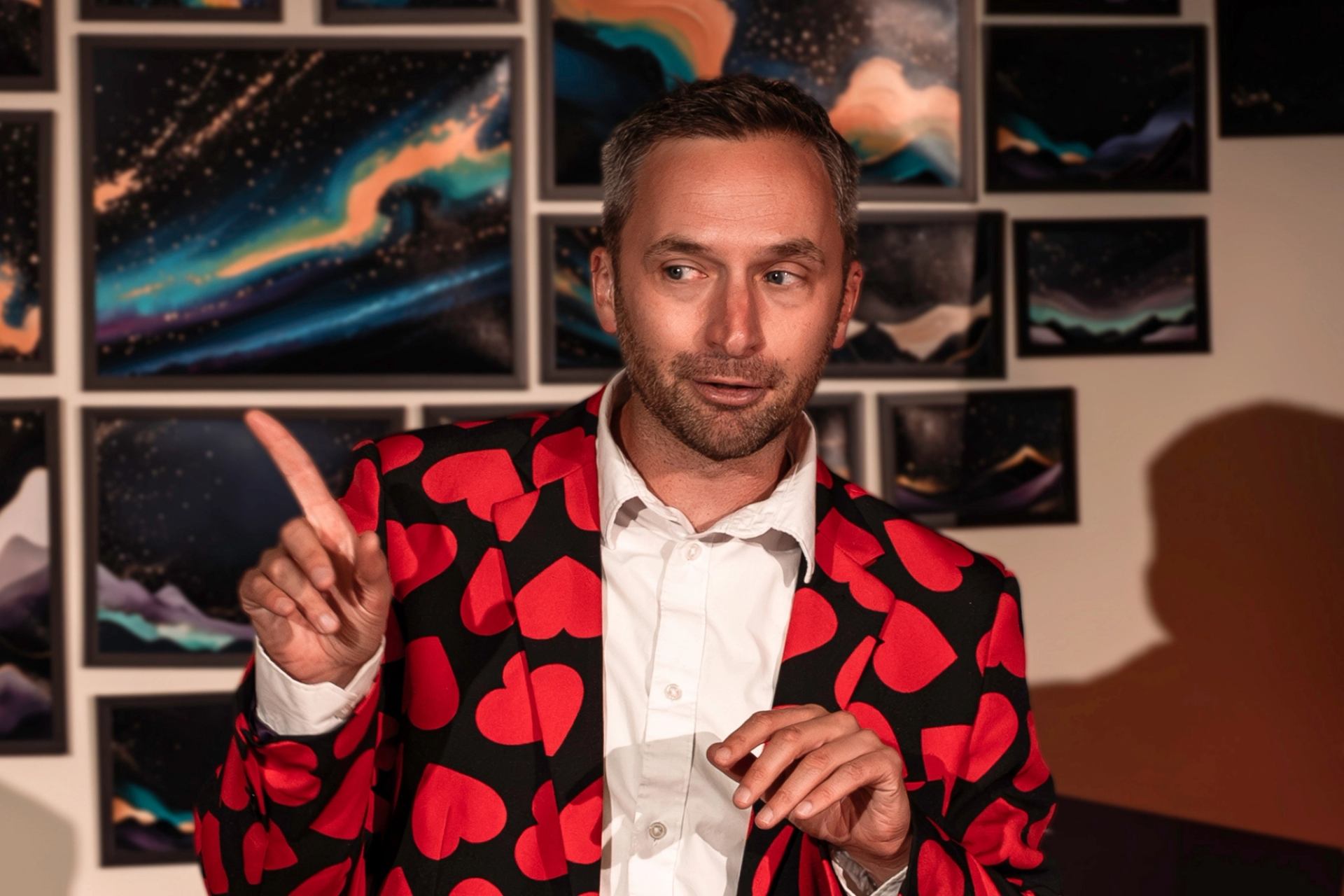 Performer in a heart‑pattern jacket speaking animatedly onstage