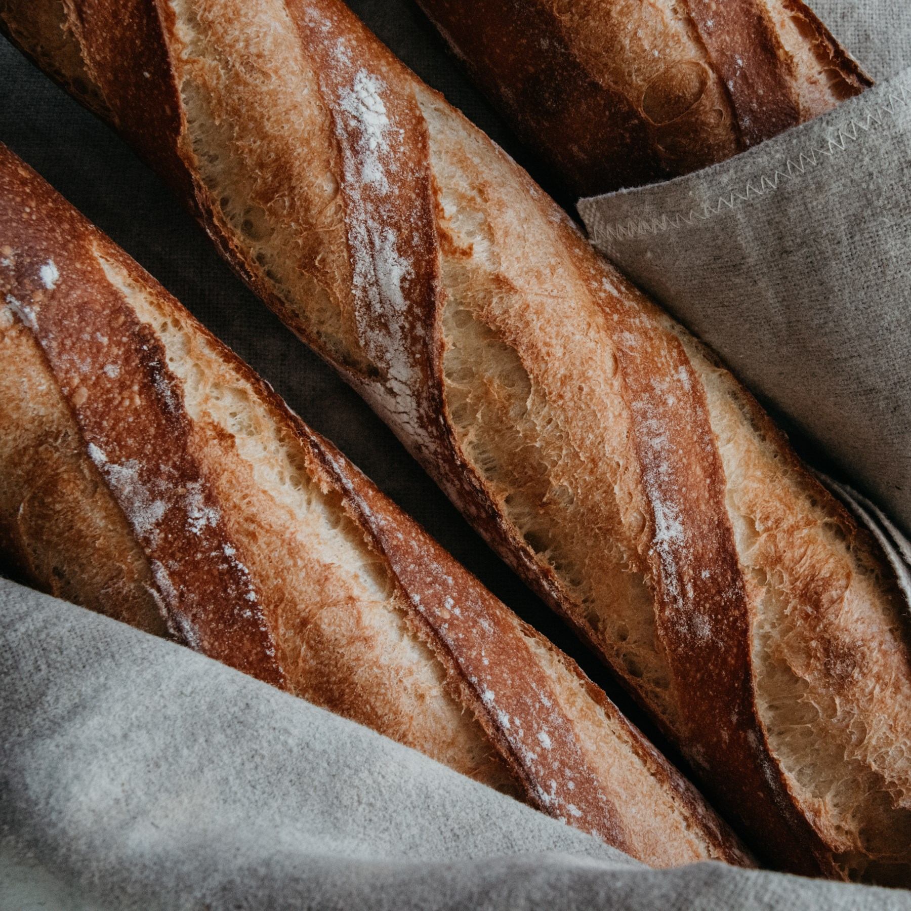 Fresh loaves of bread with flour dusting on grey parchment liners.